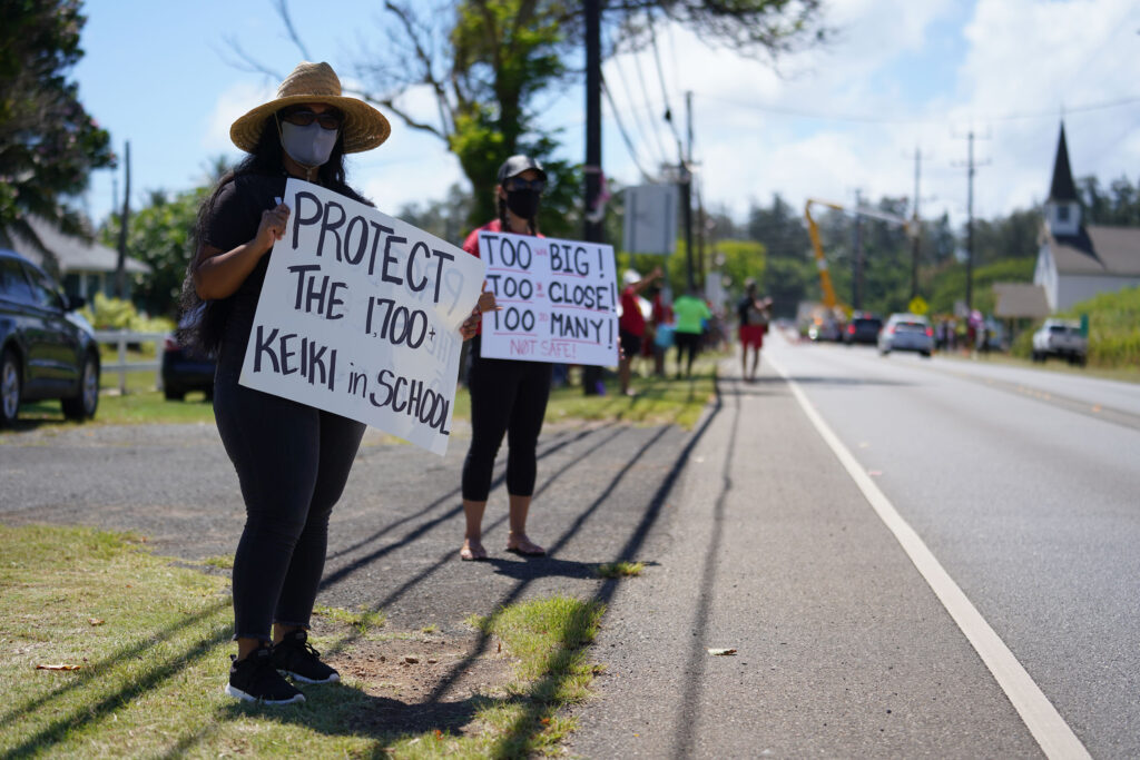 Laie resident, Sonnie Muaina and right, Oriana McCallum from Kahuku hold signs along Kamehameha Highway in Kahuku against the windmills.